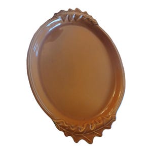 May include: A large, oval-shaped serving platter with a brown glaze. The platter has two leaf-shaped handles on either side.
