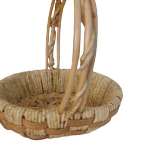 May include: A small, round wicker basket with a woven handle. The basket is made of natural, light brown wicker.