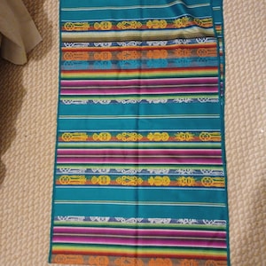 May include: A teal fabric with colorful stripes and geometric patterns. The fabric has a woven texture and is likely used for a blanket or throw.