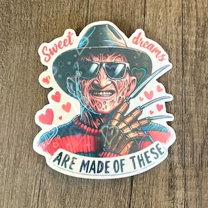 May include: A sticker featuring a cartoon illustration of Freddy Krueger from the movie A Nightmare on Elm Street. The sticker has a red and white striped sweater, a brown hat, and a glove with blades. The text on the sticker reads "Sweet dreams are made of these".