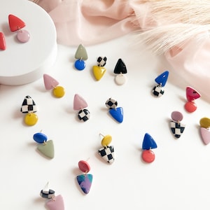 May include: A collection of colorful geometric earrings. The earrings feature various shapes, including triangles and circles, in shades of red, pink, yellow, blue, black, and white. Some earrings have a checkered pattern.