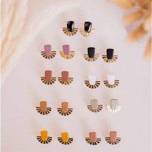 May include: A collection of handmade earrings in various colors, including black, pink, brown, white, orange, and green. Each pair features a rectangular top and a fan-shaped brass base. The earrings are displayed on a light background.