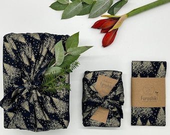 Puede incluir: Tres envoltorios de regalo de tela con fondo negro y un patrón de árboles de purpurina dorada. La tela está atada con una cinta negra y una etiqueta marrón con el texto "Japanese Furosihiki" impreso en ella.