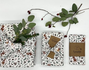 Può includere: Tre confezioni regalo in tessuto bianco con stampa di animali del bosco. Il tessuto è legato con un nodo e presenta un'etichetta di carta marrone con il testo "Sakana Furosihiki" stampato su di essa.