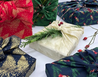Puede incluir: Varios regalos envueltos con telas festivas. Las telas presentan patrones dorados de árboles y pájaros sobre fondos rojos, verdes, azul marino y crema. Algunos están adornados con ramitas de vegetación y bayas, creando un tema navideño.
