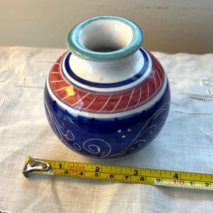 May include: A small, round, blue and white ceramic vase with red and green accents. The vase has a swirling design and is approximately 6 inches tall.