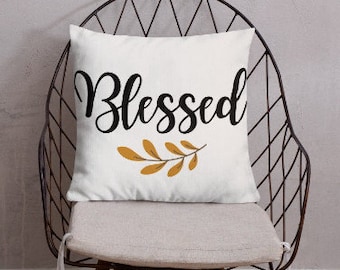 May include: White throw pillow with the word "Blessed" in black script and a gold leaf design. The pillow is on a black metal chair with a white cushion.