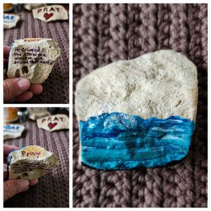 Puede incluir: Tres piedras pintadas con la palabra "Pray" y un coraz&oacute;n en cada una. Una piedra tiene una escena de oc&eacute;ano azul pintada en ella. Las otras dos piedras tienen el texto "He calmed the storm to a whisper and stilled the waves" escrito en ellas.