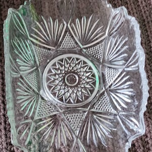 May include: A clear glass serving dish with a scalloped edge and intricate cut-glass design. The center of the dish features a large, starburst pattern.