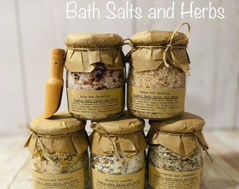 May include: Six glass jars filled with bath salts and herbs, labeled with different scents and ingredients. The jars are arranged in a pyramid shape on a wooden surface. The jars are topped with brown paper and twine.