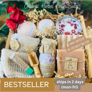 May include: A gift basket filled with organic bath products, including bath bombs, bath salts, soap, and a lip balm. The basket is made of natural materials and is decorated with dried flowers. The text "HAND-CRAFTED BY MY ZERO WASTE FAM STORE" is visible on a tag attached to the basket.