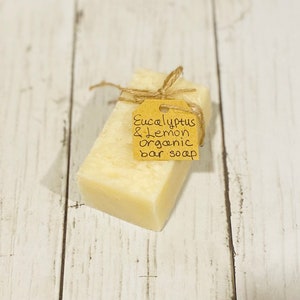 Puede incluir: Una barra de jab&oacute;n org&aacute;nico con una etiqueta de papel marr&oacute;n atada alrededor. La etiqueta dice "Eucalyptus & Lemon organic bar soap".