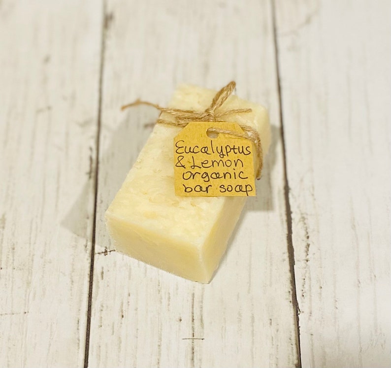 Puede incluir: Una barra de jab&oacute;n org&aacute;nico con una etiqueta de papel marr&oacute;n atada alrededor. La etiqueta dice "Eucalyptus & Lemon organic bar soap".