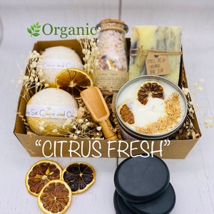 May include: A gift basket with a citrus theme. It includes bath bombs, bath salts, a bar of soap, a candle, and black massage stones. The basket is made of brown cardboard and has a white background. The text "CITRUS FRESH" is printed on the front of the basket.