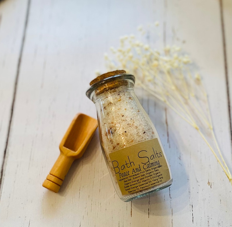 May include: A glass jar with a cork lid filled with bath salts. The jar has a brown paper label with the text "Bath Salts Peace And Calming" and a list of ingredients.