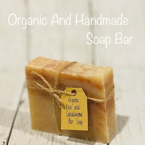 Pu&ograve; includere: Una saponetta biologica alla rosa e al sandalo, avvolta in spago con un'etichetta di carta marrone su cui &egrave; scritto "Organic Rose and Sandalwood Bar Soap".