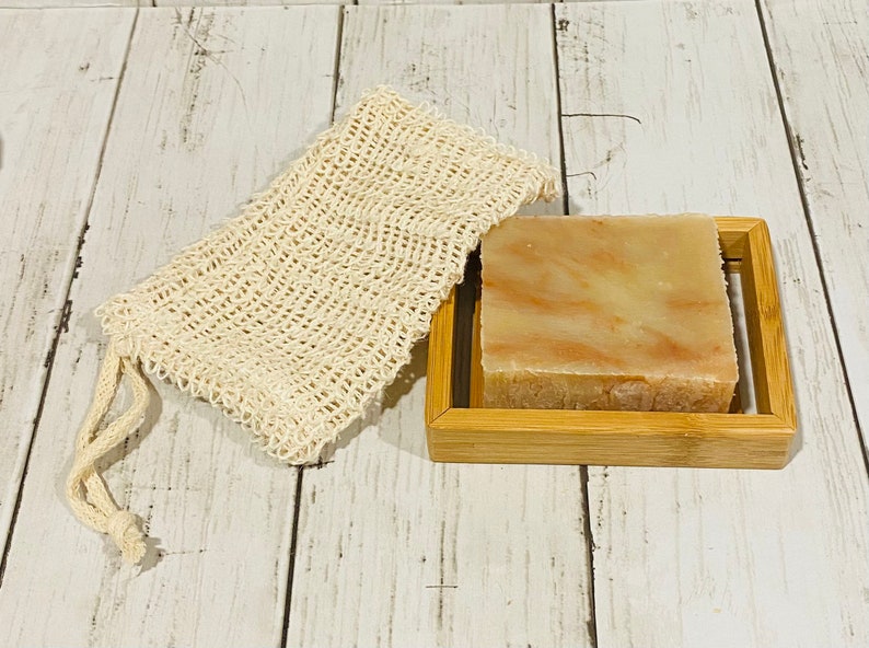 Pu&ograve; includere: Una saponetta naturale con un aspetto marmoreo in tonalit&agrave; di marrone e arancio, appoggiata su un portasapone in bamb&ugrave;. &Egrave; inclusa anche una sacca per sapone in rete bianca.