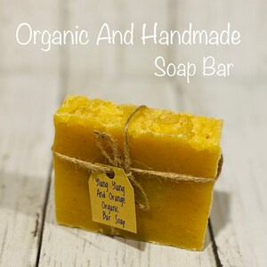 Pu&ograve; includere: Una saponetta biologica fatta a mano con un'etichetta di carta marrone che recita "Ylang Ylang And Orange Organic Bar Soap". Il sapone &egrave; di colore giallo brillante ed &egrave; legato con uno spago.