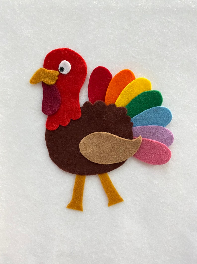 Pu&ograve; includere: Decorazione di tacchino in feltro colorato. Il tacchino ha una testa rossa, un corpo marrone e un ventaglio di piume arcobaleno. Presenta un becco, bargigli e zampe gialle. Un oggetto artigianale festivo per il Ringraziamento.