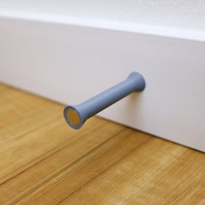 May include: A gray plastic door stop with a gold metal base attached to a white wall.