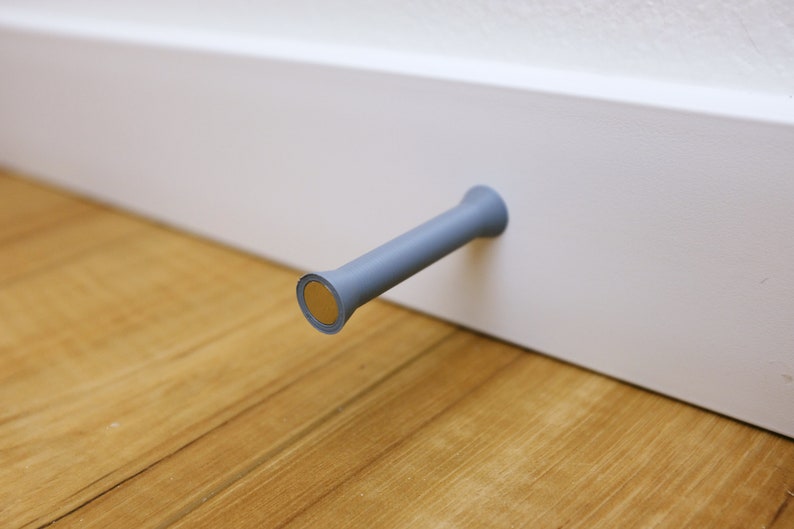 May include: A gray plastic door stop with a gold metal base attached to a white wall.
