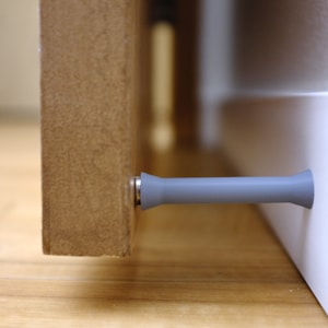 May include: A gray doorstop with a rounded end, attached to a wooden door.