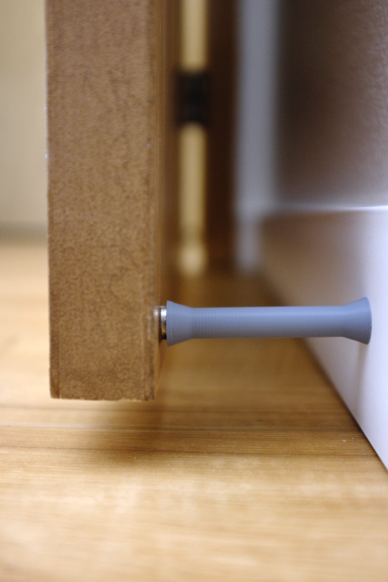 May include: A gray doorstop with a rounded end, attached to a wooden door.