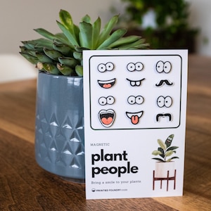 May include: A set of magnetic plant face stickers with various expressions, including eyes, mouths, and mustaches. The card reads "plant people" and "Bring a smile to your plants".