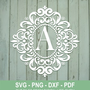 Op de afbeelding: Witte monogramletter A met een decoratief, versierd frame. De letter is gecentreerd in het frame. Het frame is gemaakt van spiralen en krulletjes. De achtergrond is een lichtgroene houtstructuur.