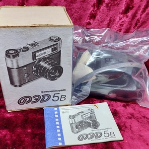 May include: A vintage camera in its original box with a black leather strap and instruction manual. The camera is a black and silver Fed 5B, a Soviet-made rangefinder camera.