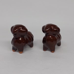 Puede incluir: Dos pequeñas figuritas de ovejas de cerámica marrón. Las ovejas están de pie sobre una superficie blanca.
