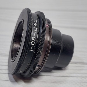 Peut inclure: Un adaptateur d'objectif d'appareil photo en métal noir avec le texte "60-1 UMI" imprimé sur le côté.