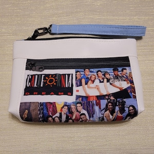 May include: White zippered pouch with a black zipper and a blue strap. The pouch has a collage of images of a group of people on a beach with the text "California Dreams" printed on the front.