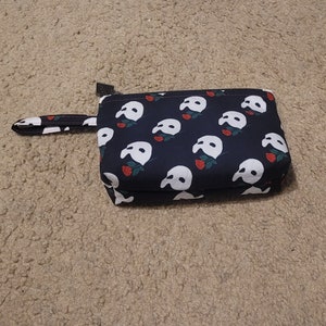 May include: A black zippered pouch with a white phantom of the opera mask and red rose pattern.