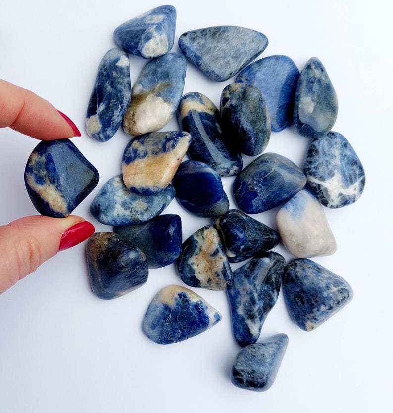 May include: A collection of tumbled blue sodalite stones. The stones are various shades of blue with white and brown markings. The stones are smooth and polished.