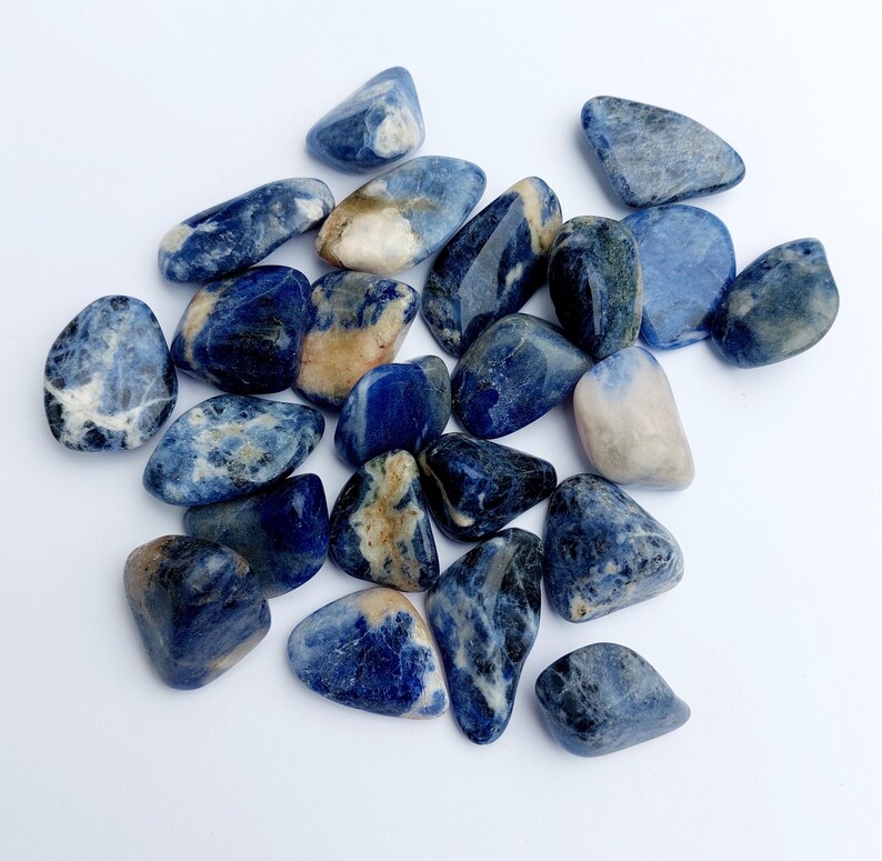 May include: A collection of tumbled blue sodalite stones. The stones are a mix of light and dark blue with white and brown markings.