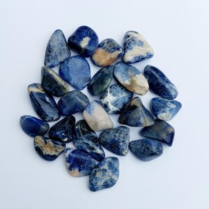 May include: A collection of tumbled blue and white sodalite stones. The stones are smooth and polished, with a variety of blue and white patterns.