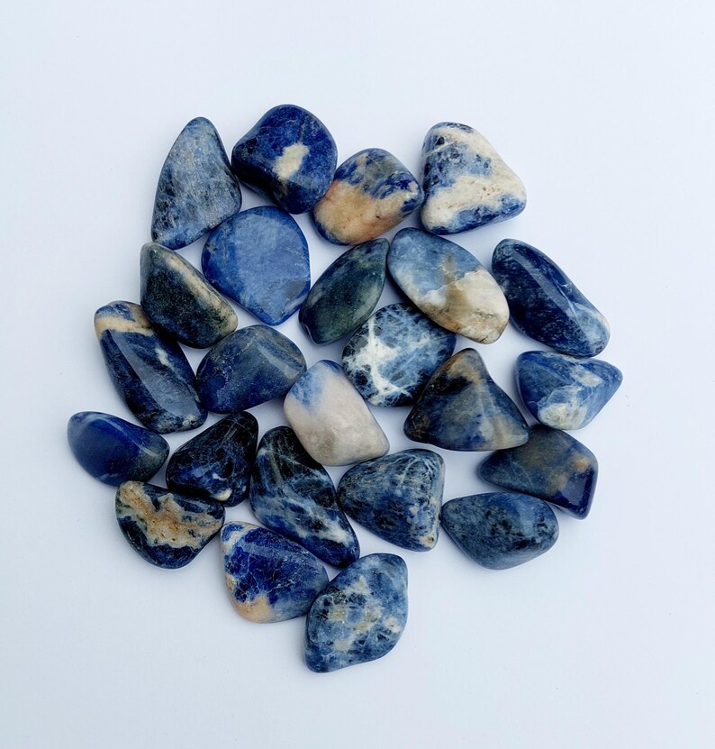 May include: A collection of tumbled blue and white sodalite stones. The stones are smooth and polished, with a variety of blue and white patterns.