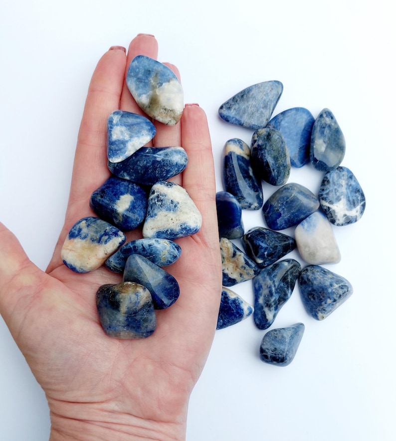May include: A collection of tumbled blue and white sodalite stones. The stones are smooth and polished, with a variety of shapes and sizes.