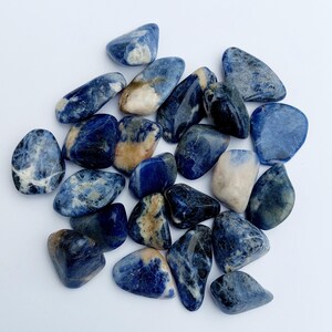 May include: A collection of tumbled blue and white sodalite stones. The stones are smooth and polished, with a variety of shapes and sizes.