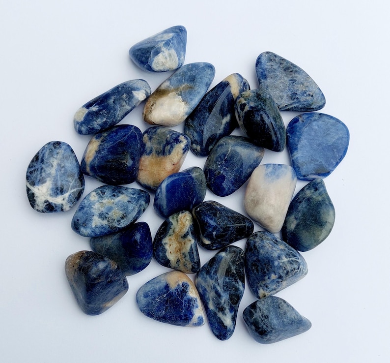 May include: A collection of tumbled blue and white sodalite stones. The stones are smooth and polished, with a variety of shapes and sizes.