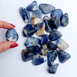 May include: A collection of tumbled blue and white sodalite stones. The stones are smooth and polished, with a variety of blue and white patterns.