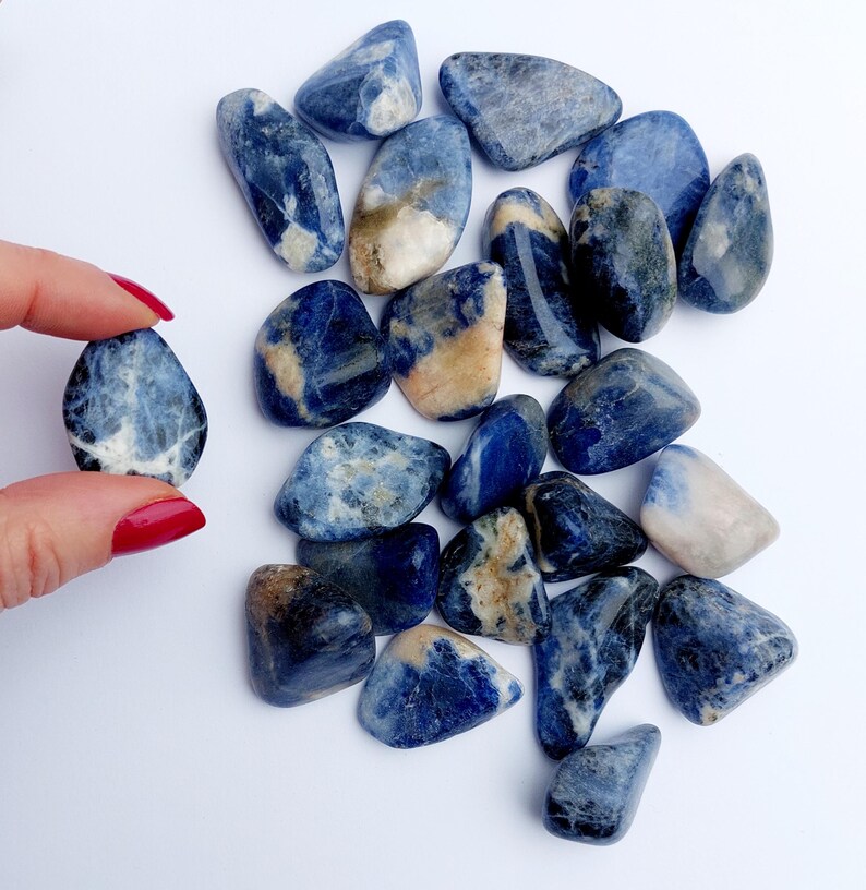 May include: A collection of tumbled blue and white sodalite stones. The stones are smooth and polished, with a variety of blue and white patterns.