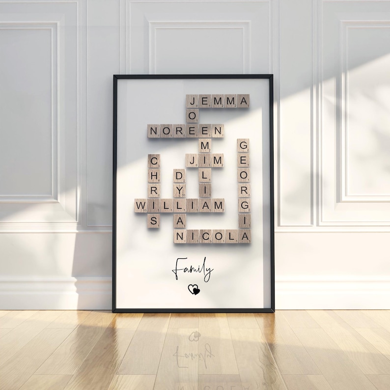 May include: A framed wall art print featuring a crossword puzzle arrangement of wooden letter tiles spelling out the names Jemma, Noreen, Jim, Chris, Dylan, William, Georgia, and Nicola. The word Family is printed below with a small heart icon.