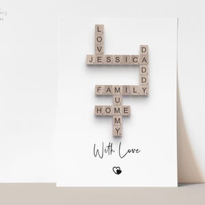 May include: A white rectangular print featuring a crossword-style arrangement of wooden letter tiles spelling LOVE, JESSICA, DADDY, FAMILY, MUMMY, and HOME. Below the tiles, the text With Love is printed in black script above a small heart icon.
