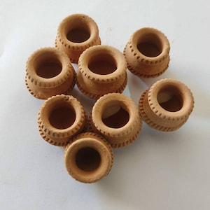 May include: Eight small, terracotta-coloured clay pots are displayed. Each pot has a rounded body, a wide, open mouth, and a decorative band of carved detail. The pots are arranged on a white surface.