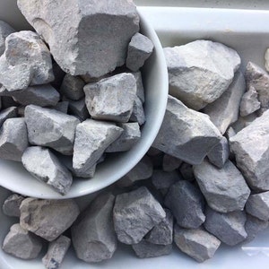 May include: A white bowl filled with gray, irregularly shaped rocks. The bowl is sitting on a white surface.