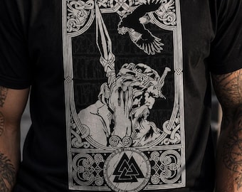 May include: Black t-shirt featuring a detailed, grayscale graphic of a Viking warrior with a spear, a raven, and the Valknut symbol. The design is framed with ornate borders. The shirt is made of a soft material.