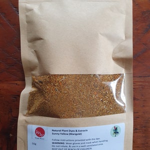 May include: A brown paper bag with a resealable zipper top contains a 50g bag of dried marigold petals. The bag has a label that reads "Natural Plant Dyes & Extracts Sunny Yellow (Marigold)" and includes instructions for use and safety warnings.