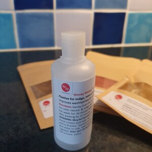 May include: A clear plastic bottle with a white cap labeled "Wonky Weaver Fixative for indigo, natural & vegetable dyes. Improves washfastness & vibrancy. Directions: Gently invert the bottle in hot water for 30 minutes after washing for 15 minutes. WARNING: May be harmful if swallowed. Avoid contact with eyes. Remove any spills with plenty of water.  Seek medical advice if ingested. KEEP OUT OF REACH OF CHILDREN. Net volume: 120ml"
